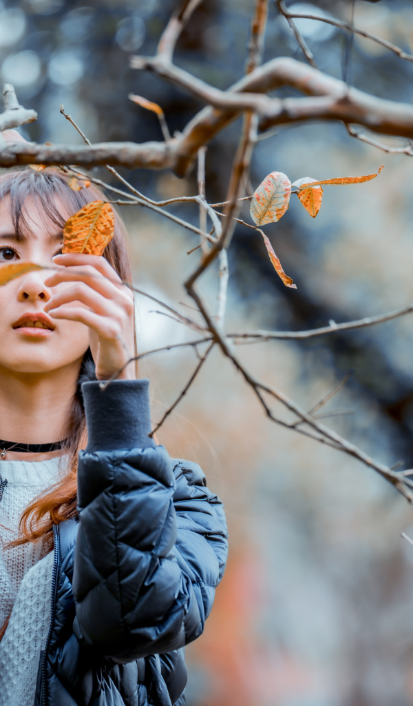 Девушка азиатка в черной куртке у дерева