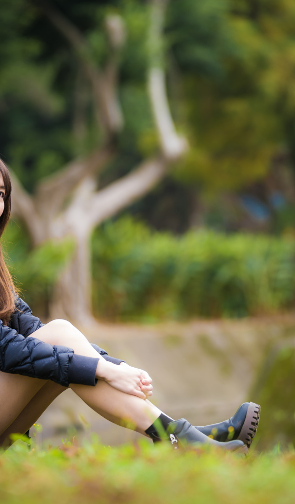 Девушка азиатка в черной куртке сидит на траве