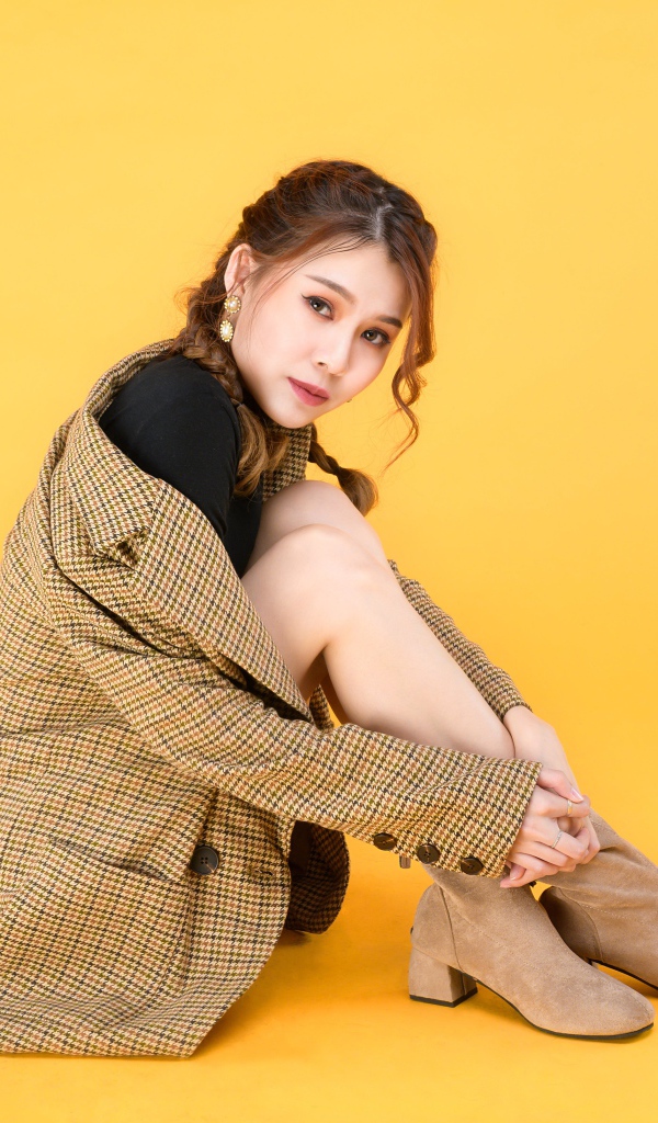 Девушка азиатка в пальто на желтом фоне 