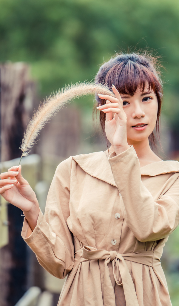 Девушка азиатка в пальто стоит у забора 