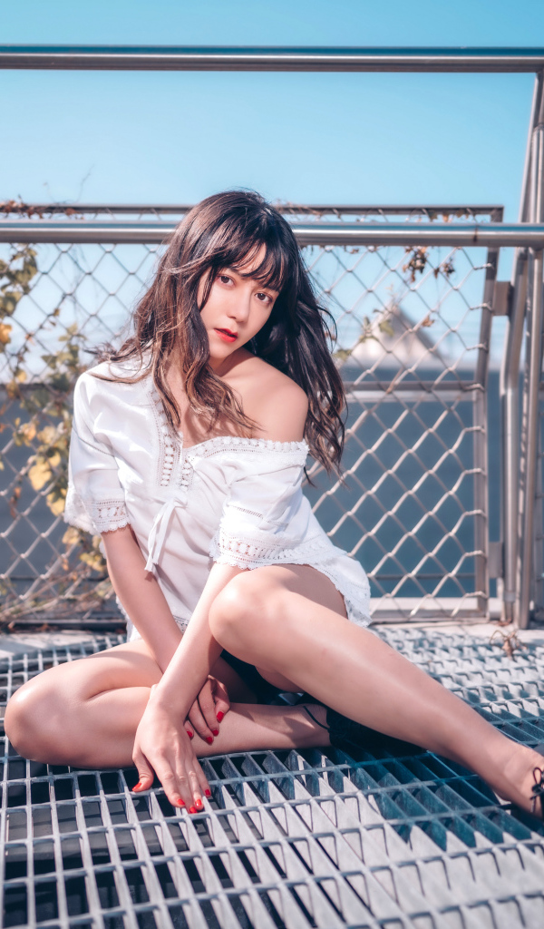 Девушка азиатка в белом наряде сидит на сетке