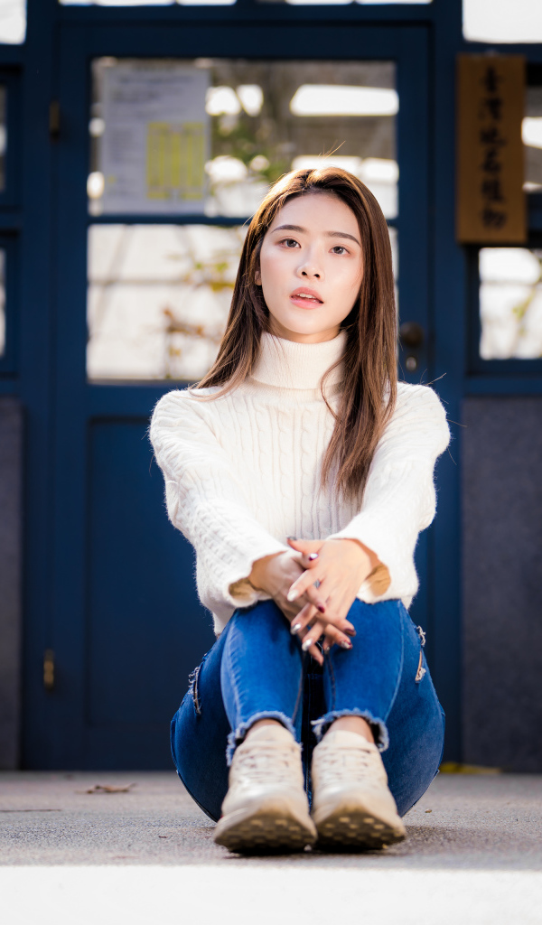 Девушка азиатка в белом свитере видит на полу 