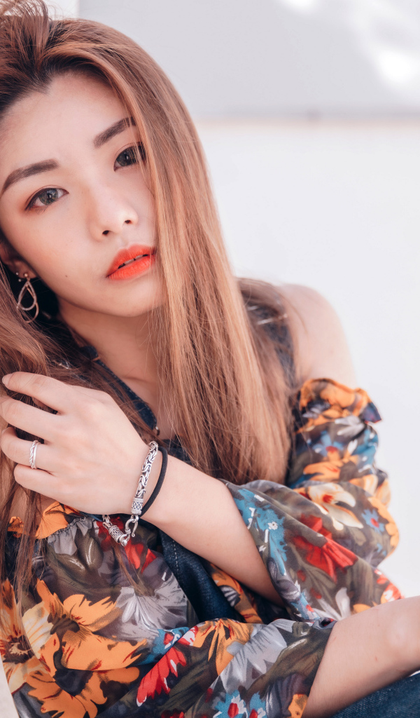 Девушка азиатка сидит на полу у стены 