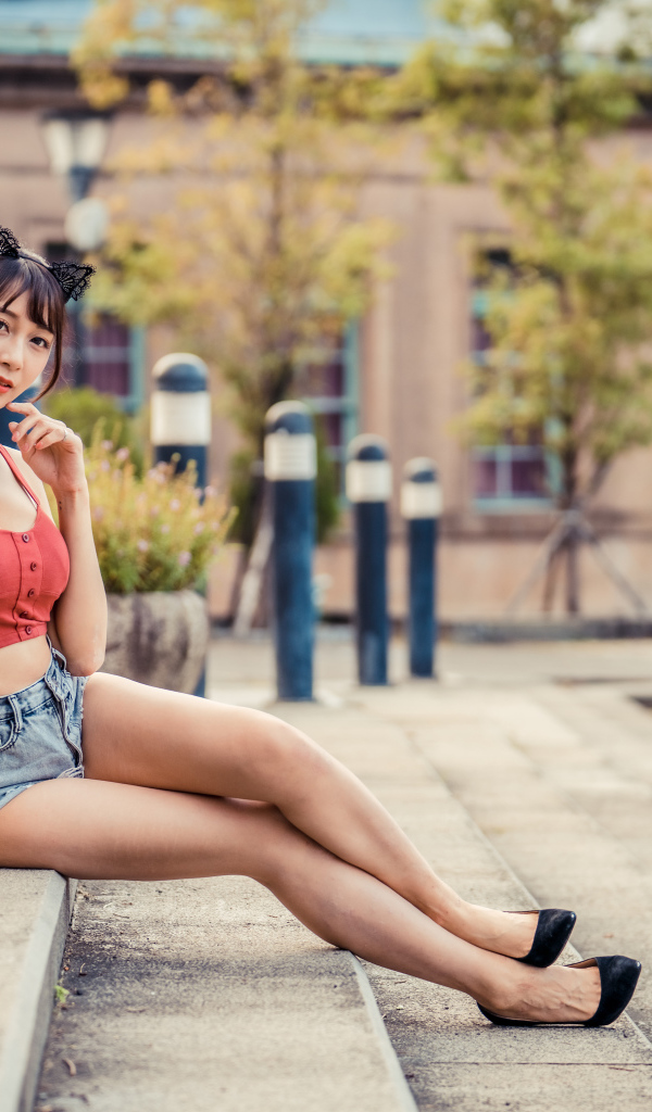 Азиатка в шортах сидит на ступенях 