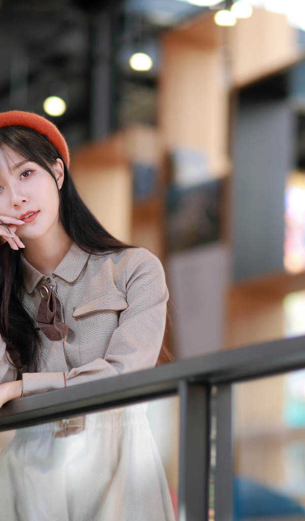 Азиатка в сером платье стоит у перил 