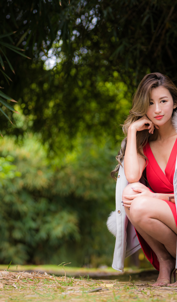 Азиатка в красном платье сидит в парке 