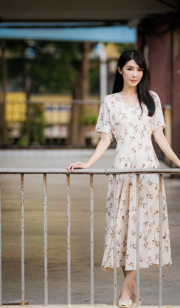 Красивая азиатка в платье стоит у перил