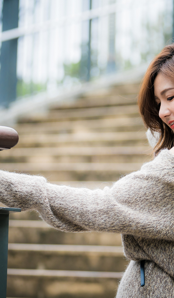 Красивая девушка азиатка в сером свитере на ступеньках 