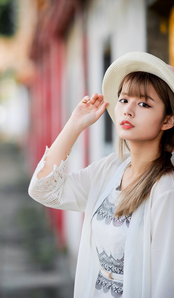 Красивая азиатка в шляпе стоит у стены