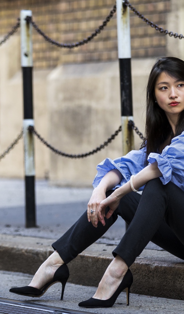 Красивая девушка азиатка в черных брюках сидит на земле