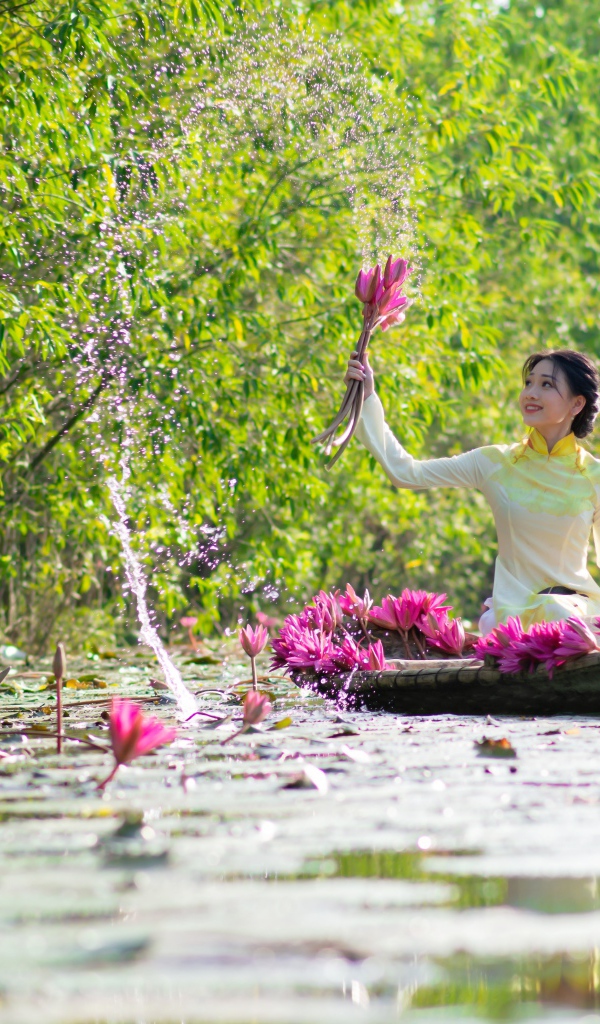 Красивая девушка азиатка на лодке рвет цветы лотоса в реке