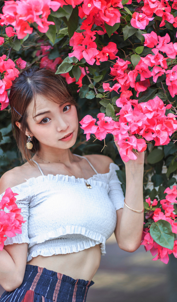 Красивая азиатка стоит у дерева с красными цветами