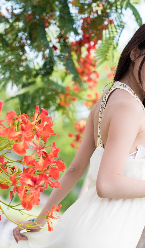 Beautiful asian girl in a red dress near a tree with flowers
