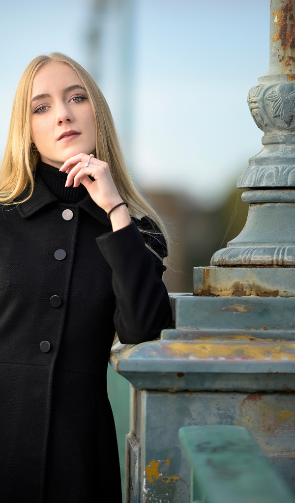 Красивая блондинка в черном пальто стоит у фонаря