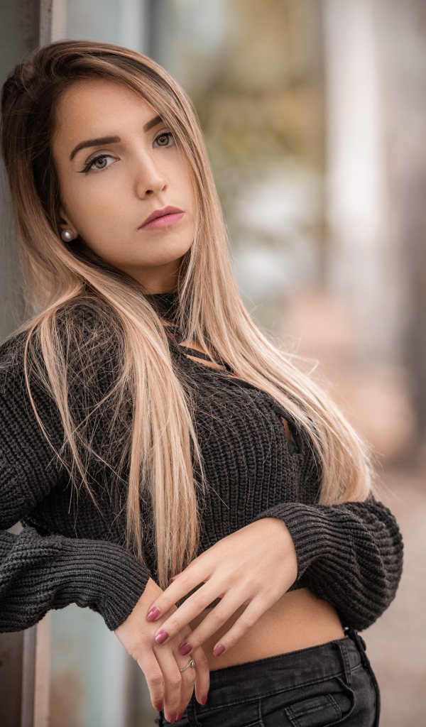 Красивая блондинка в вязаном свитере у стены 