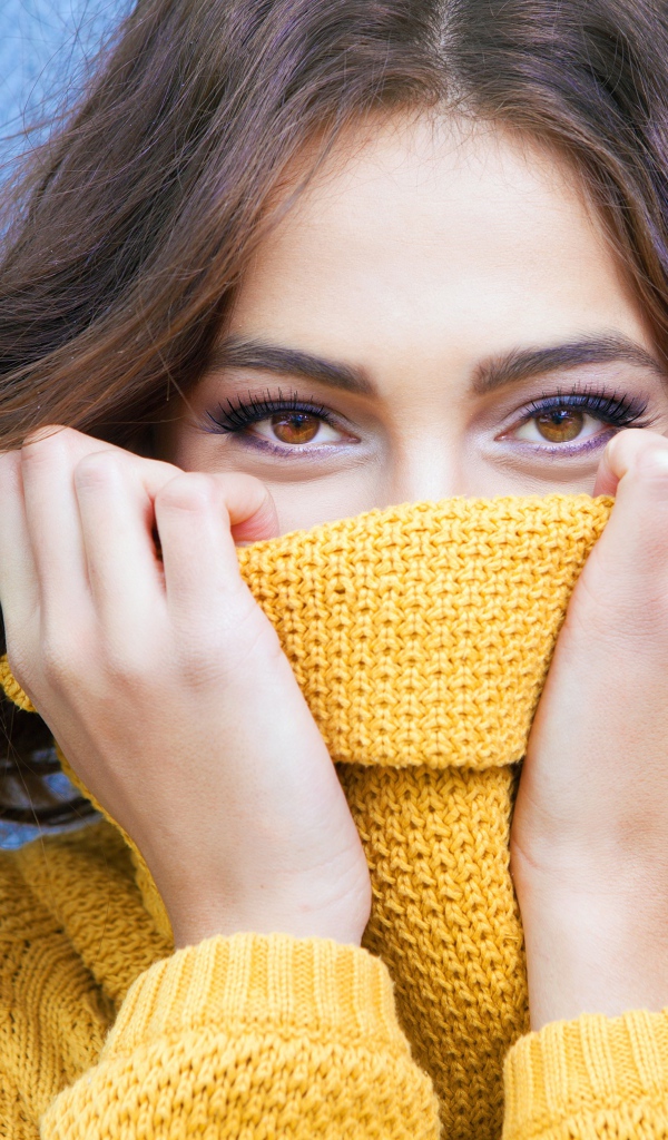 Красивая кареглазая девушка закрывает лицо свитером