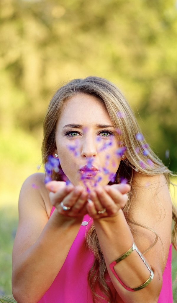 Красивая девушка сдувает лепестки с ладоней 