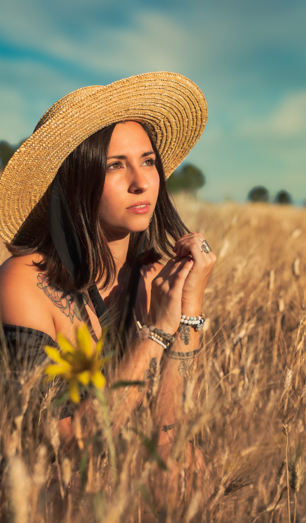 Красивая девушка в шляпе сидит на поле с пшеницей