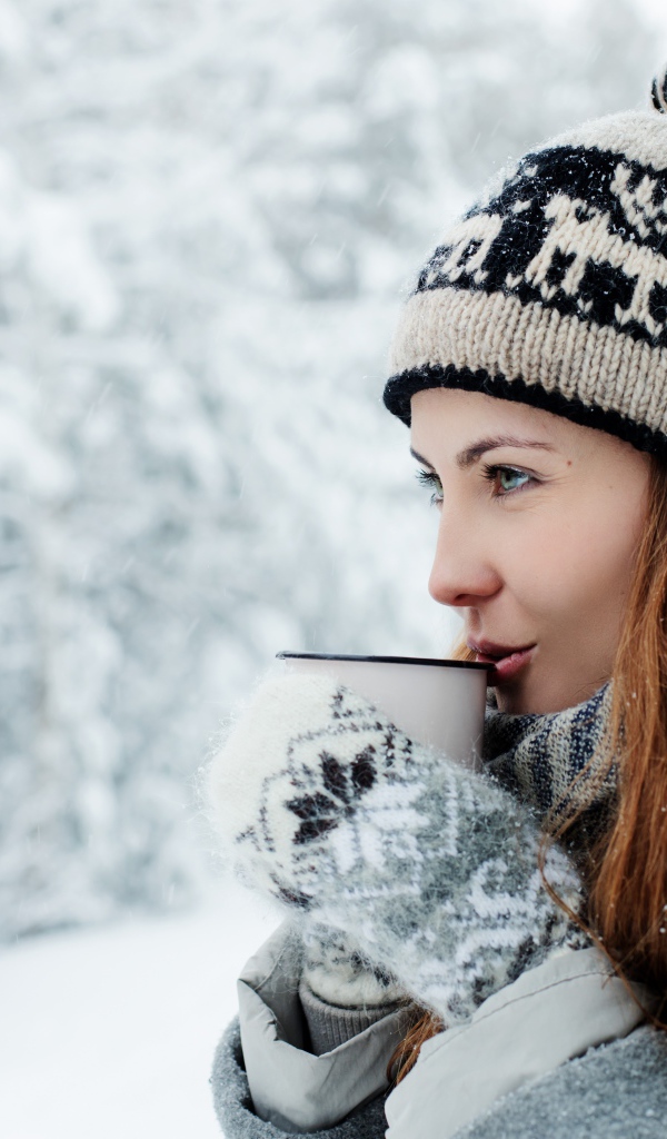 Красивая девушка в теплой шапке пьет кофе зимой на улице 