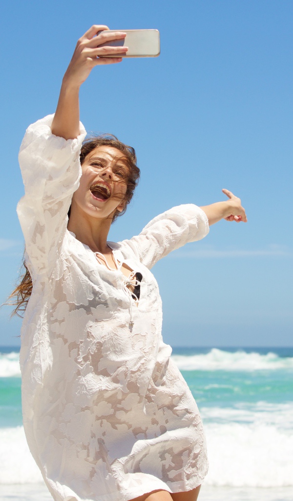 Красивая девушка в белом платье делает селфи на море 