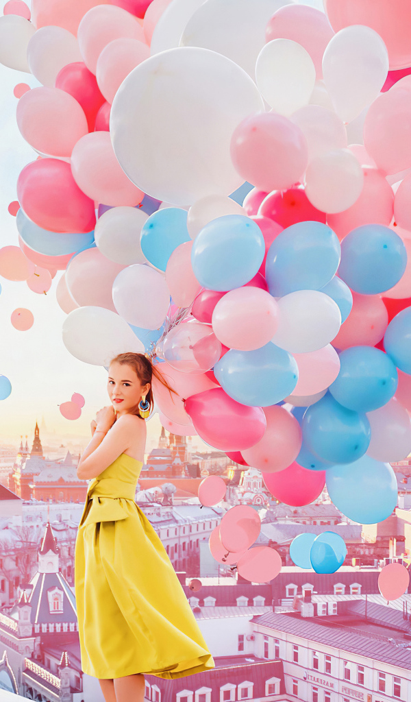 Красивая девушка в желтом платье стоит на крыше с воздушными шариками