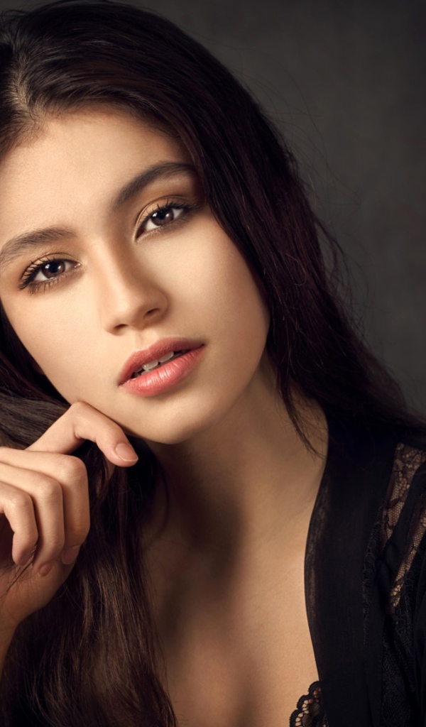 Красивая девушка в черном сидит на сером фоне