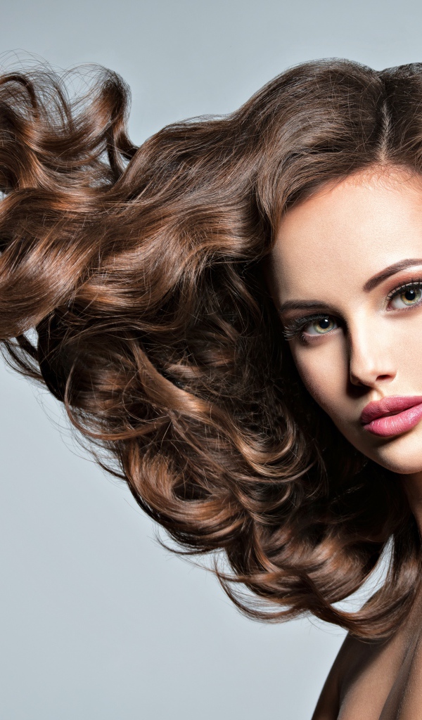 Красивая девушка модель с волнистыми волосами на сером фоне