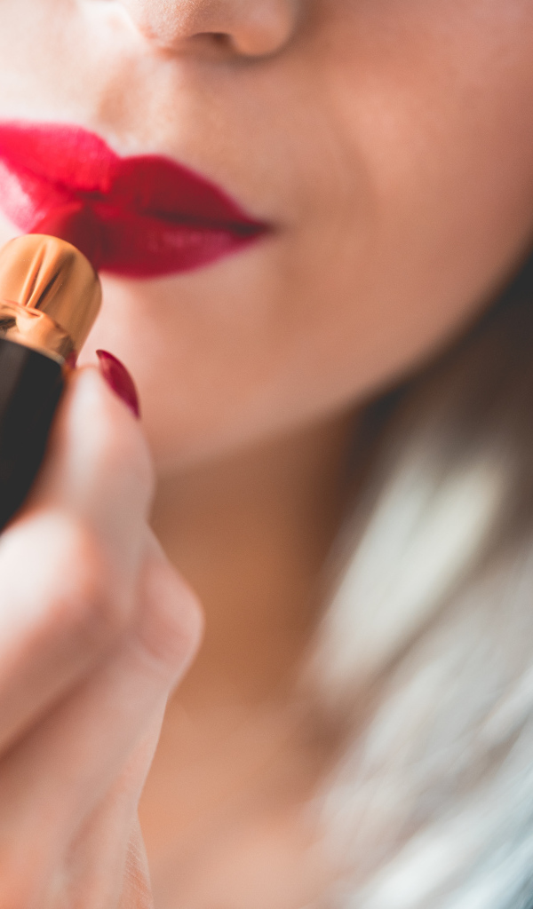 Красивая девушка красит губы красной помадой 