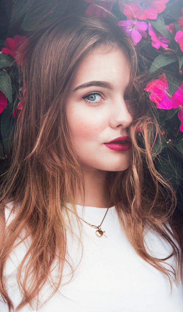 Красивая девушка стоит у зарослей с розовыми цветами