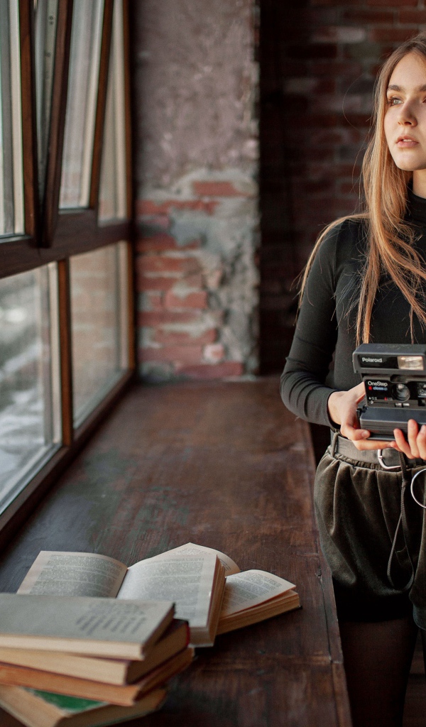 Красивая девушка с фотоаппаратом в руках у окна 