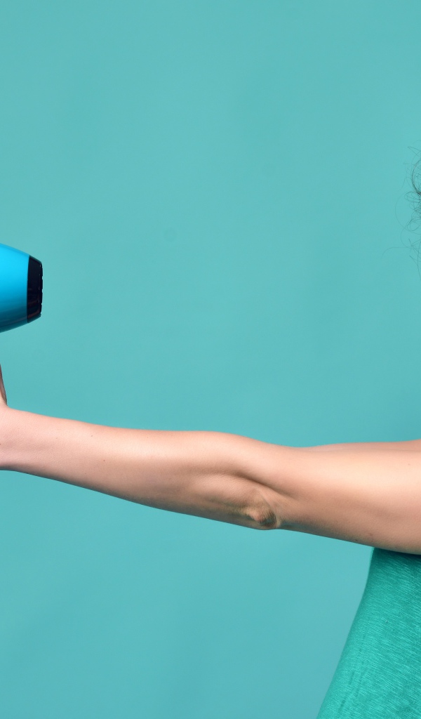 Красивая девушка с феном в руках на голубом фоне