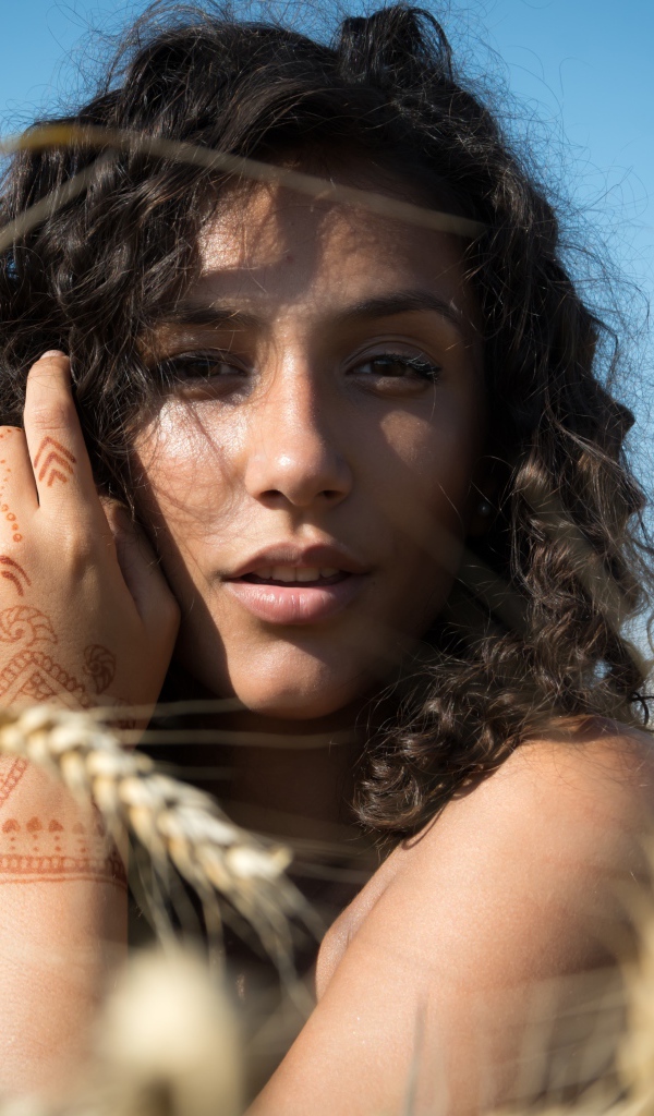 Красивая девушка с рисунком мехенди на руке на пшеничном поле 