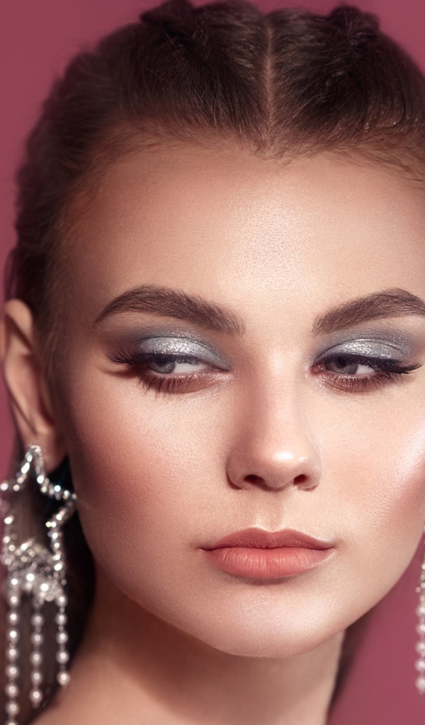 Красивая девушка с макияжем и большими серьгами на розовом фоне