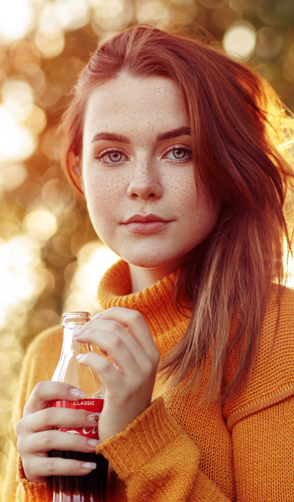 Красивая рыжеволосая девушка с бутылкой кока колы в руке 