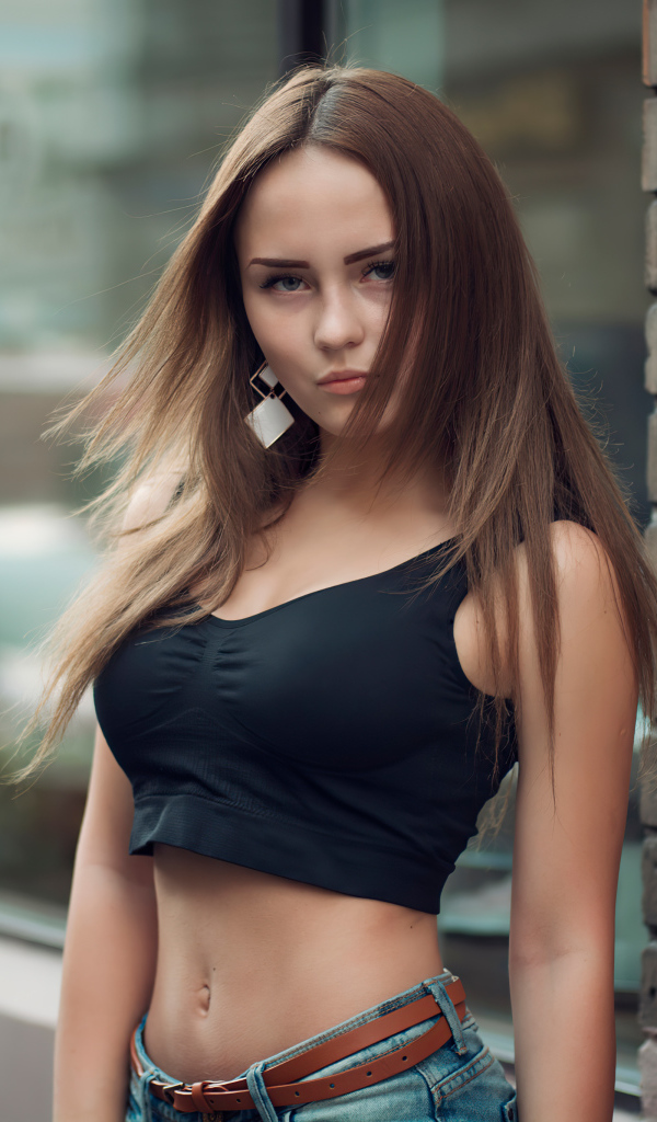 Красивая стройная девушка в черном топе стоит у стены