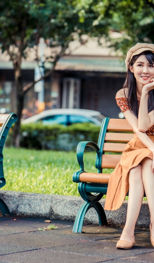 Красивая улыбающаяся азиатка сидит на лавке в парке