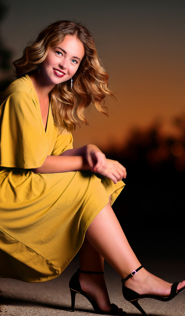 Красивая улыбающаяся девушка в желтом платье сидит на лавке 