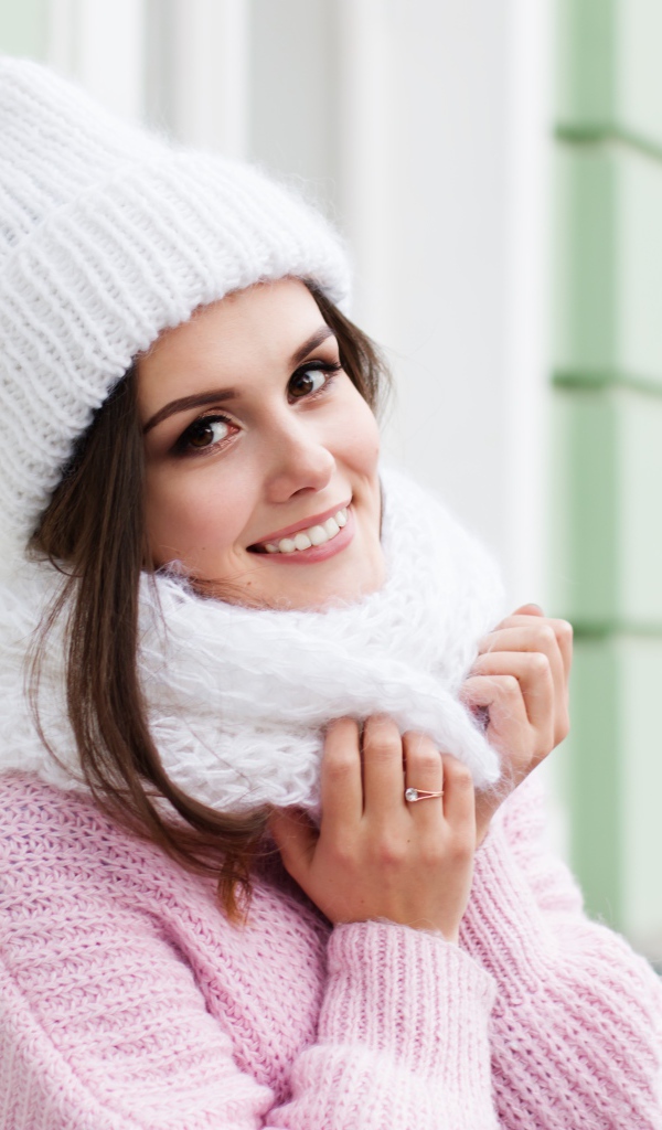 Красивая улыбающаяся девушка в розовом свитере и теплой шапке 