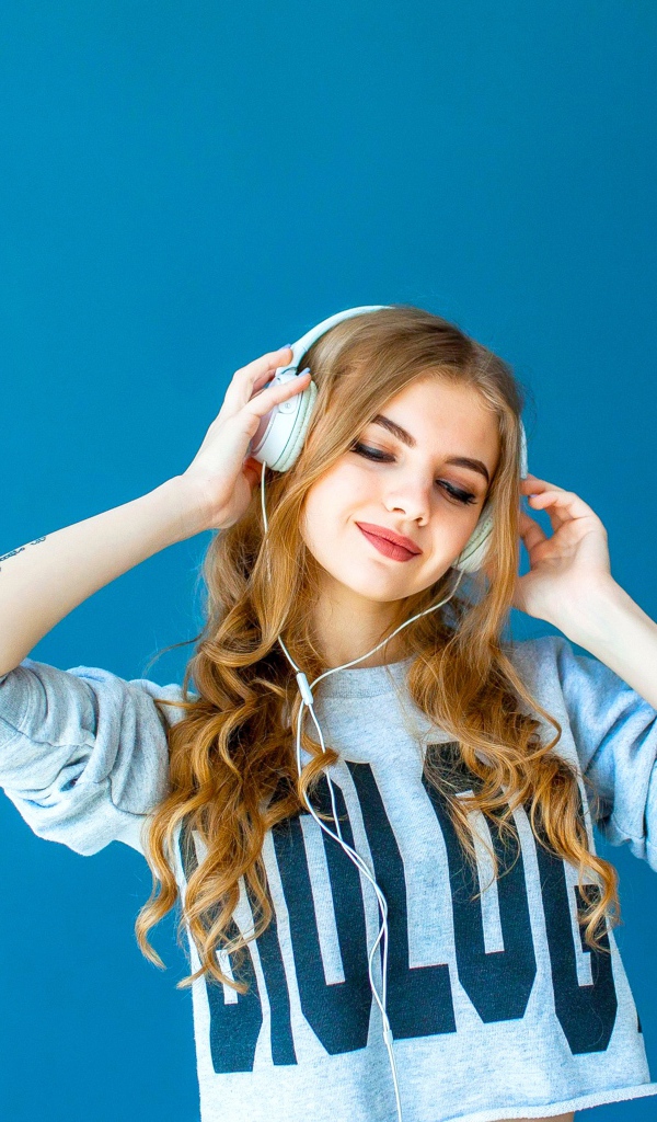 Красивая молодая девушка в наушниках на голубом фоне
