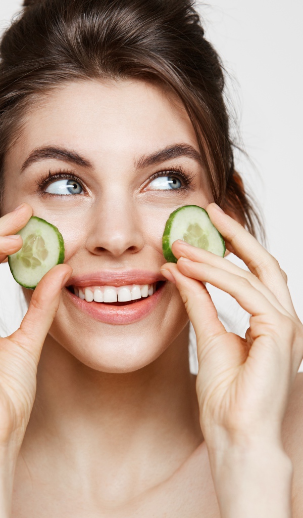 Голубоглазая девушка прикладывает огурцы к лицу 