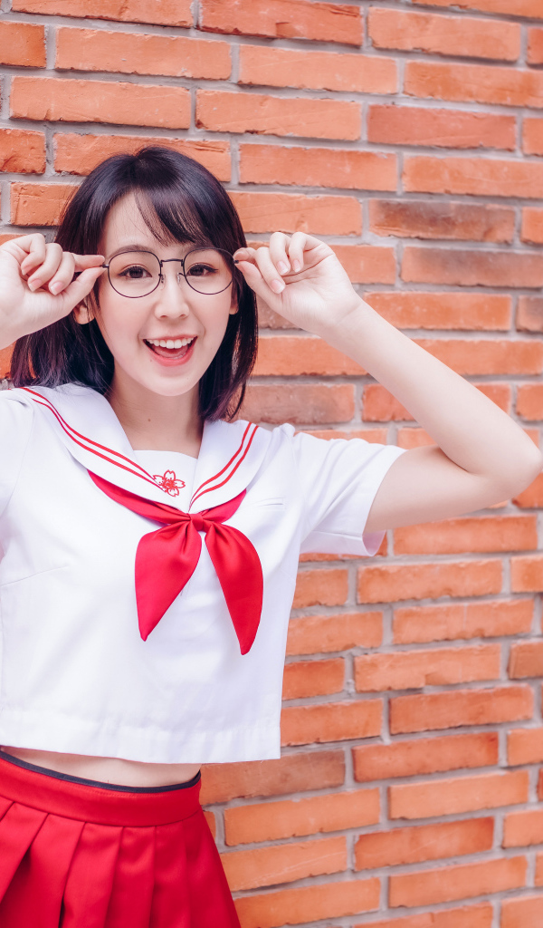 Яркая веселая азиатка в очках у кирпичной стены