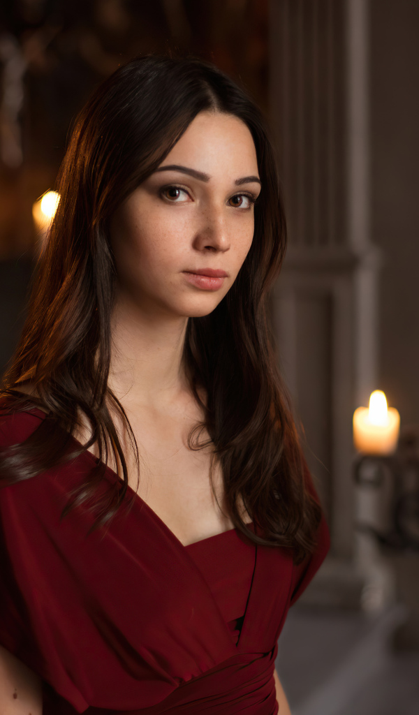 Кареглазая девушка в красном платье в комнате со свечами