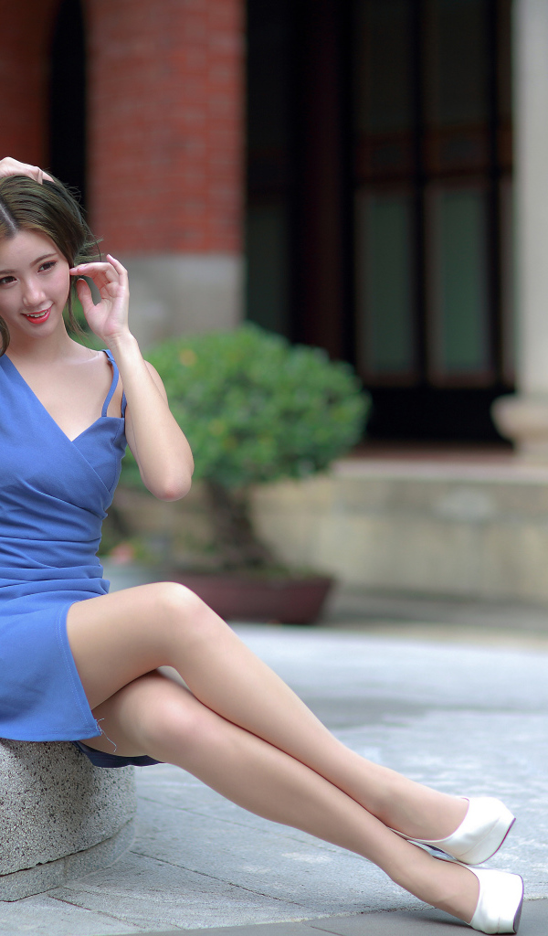 Милая девушка азиатка в голубом платье сидит у клумбы 