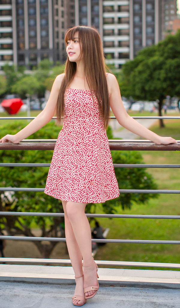 Милая девушка азиатка в платье стоит у перил 