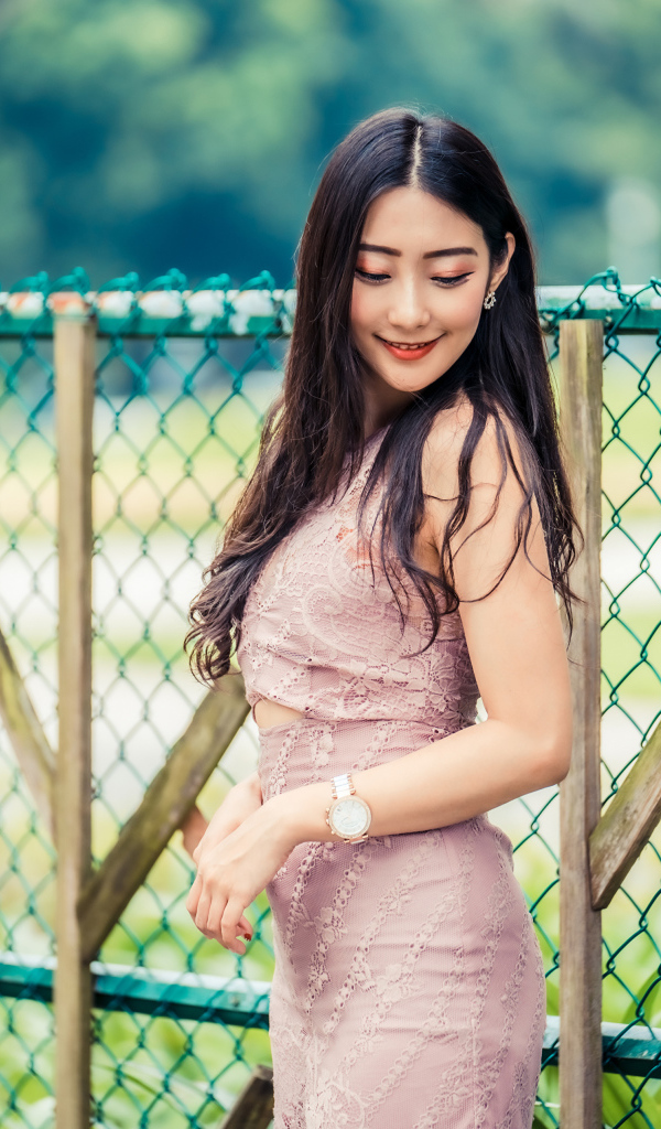 Милая азиатка в платье стоит под забором