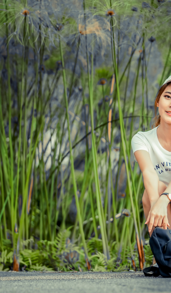 Милая девушка в кепке сидит на дороге с рюкзаком