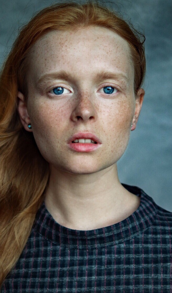 Милая рыжеволосая голубоглазая девушка с веснушками на лице на сером фоне