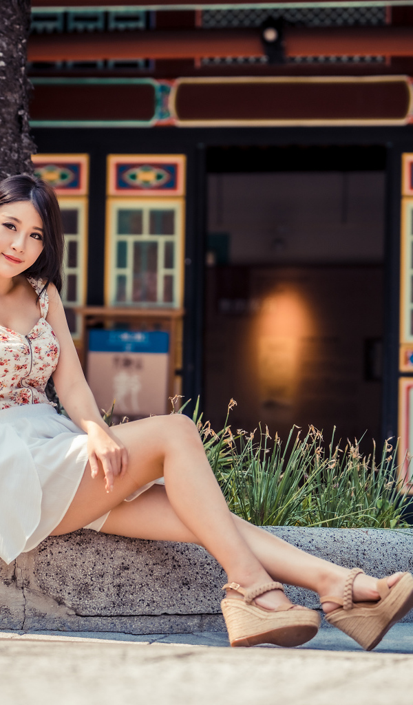 Милая улыбающаяся девушка сидит на бордюре