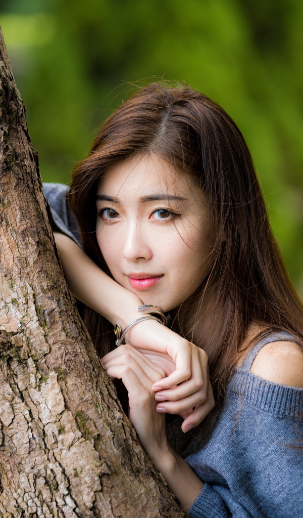 Мечтательная девушка азиатка стоит у дерева