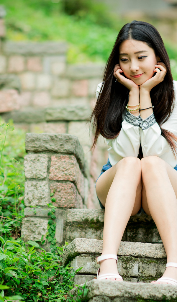Мечтательная девушка азиатка сидит на ступеньках 